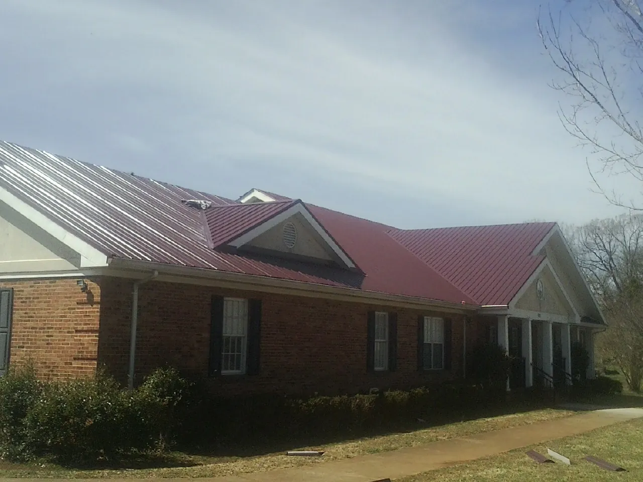 Red metal roof with gabled entries on a long brick building, from a Hail Damage Roof Repair job in Beaver Dam