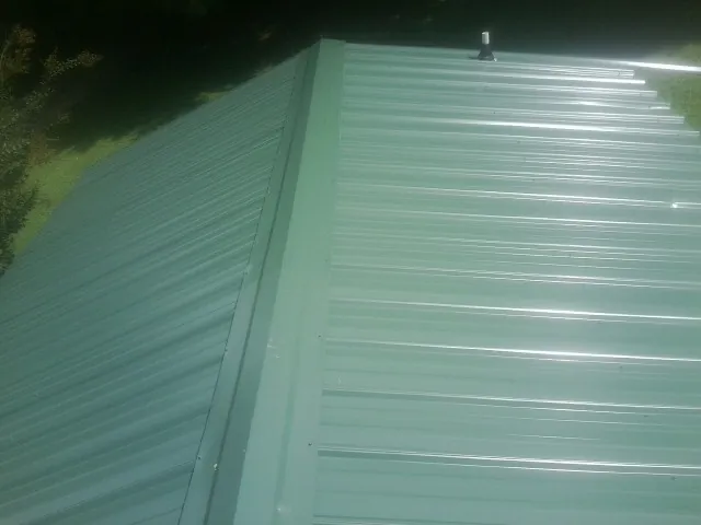 New green metal panels meeting at the ridge of a roof — Flat Roof Repair work by our crew in Beaver Dam