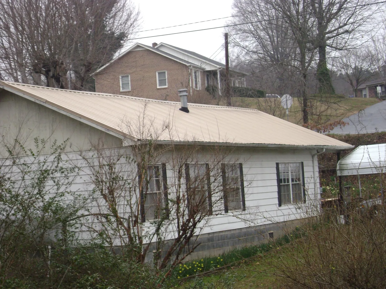 Tan metal roof on a white sided house set into a hillside — Commercial Roofing by Roofing Brothers in Beaver Dam