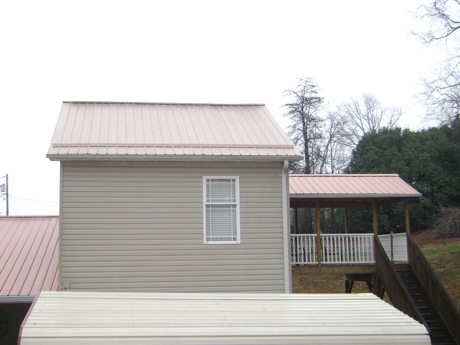 Tan metal roofs on a two story addition and attached porch, from a Roof Replacement job in Beaver Dam