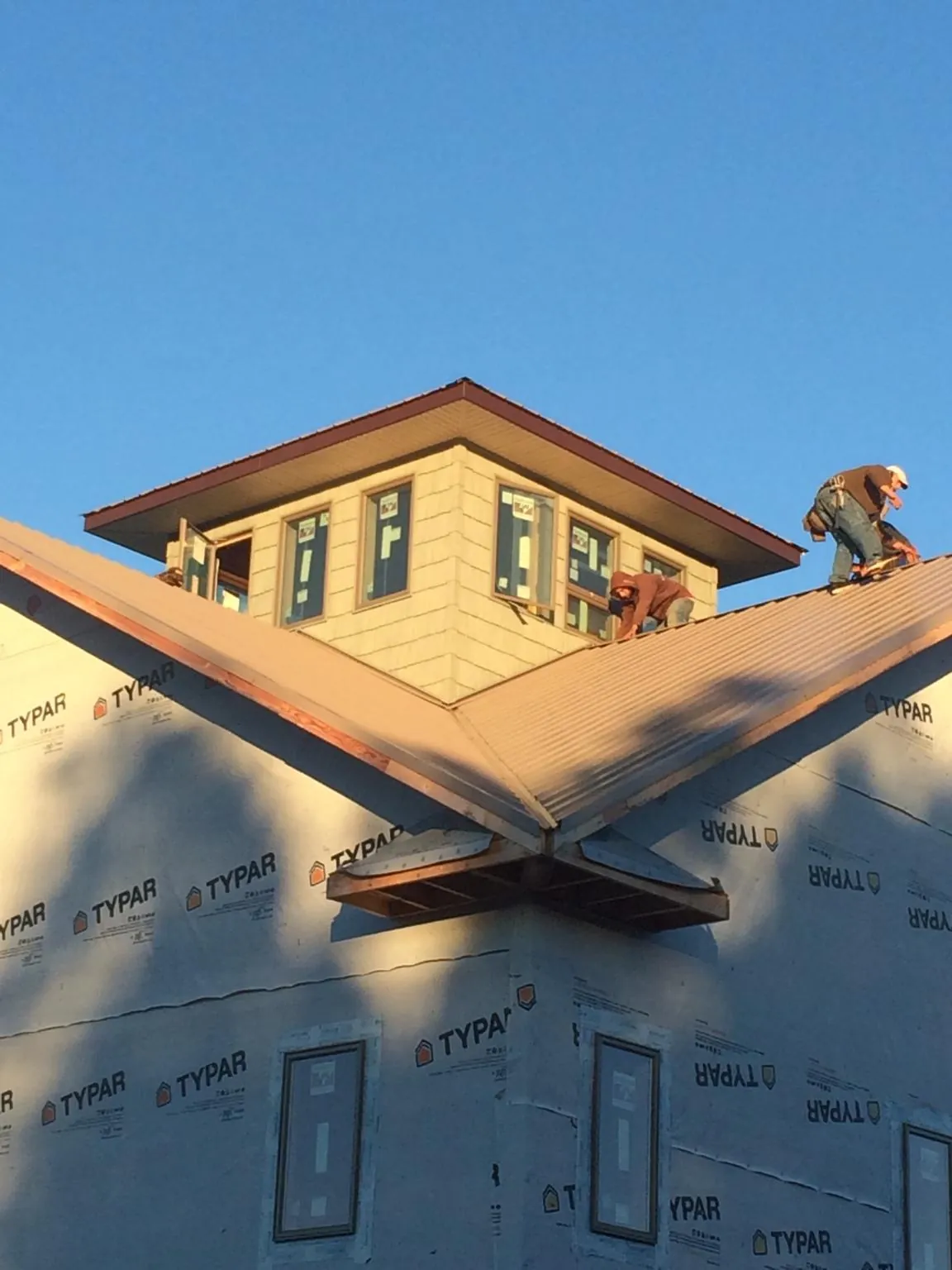 Roofers working around a rooftop cupola on a new metal roof at sunset — Roof Waterproofing in Beaver Dam by Roofing Brothers